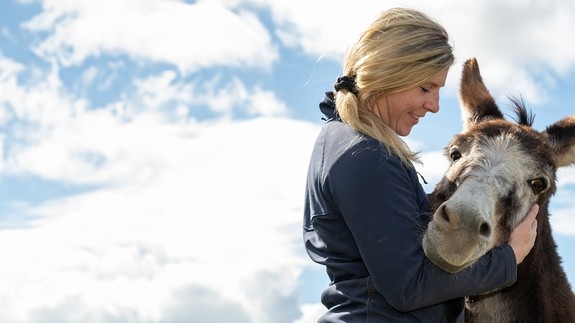 A women lovingly holding a white and brown donkeys face