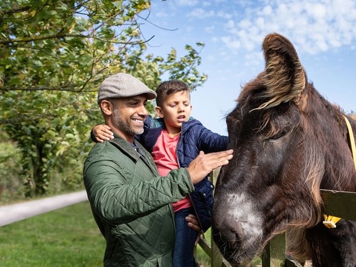 A father holding his son as the stoke a dark brown donkey